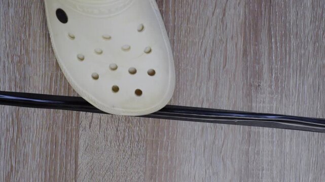 Walking over taped cable unsurety. Casual shoes traverse taped wire during home movement. Everyday scene showing foot carefully over taped cord to prevent fall hazards