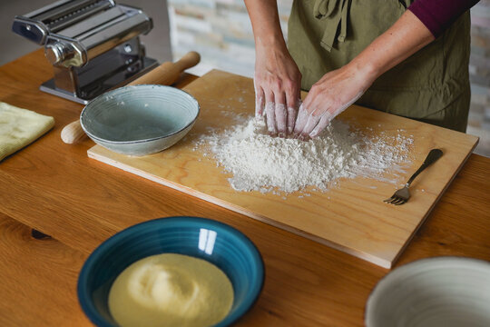 Young woman preparing flour for homemade pasta dought indoor - Italian culture, healthy food and lifestyle concept