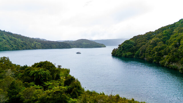 Aerial view of a boat sailing through the calm, deep blue waters, framed by lush green hills under a soft, overcast sky, Marlborough, New Zealand.