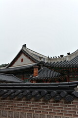 Fototapeta premium Traditional Korean Palace Rooftops with Guardian Figurines on Ridge, Decorative Gable Wall, Brick Chimney and Dancheong Ornaments Against Cloudy Sky, Seoul, South Korea