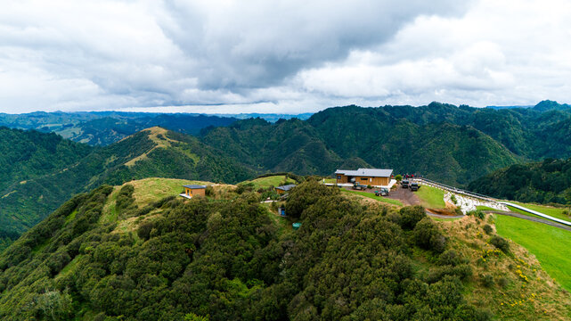 Aerial view of The Chef's Table at Blue Duck Station amidst rolling hills, a vivid tapestry of green and brown under a dramatic sky, Retaruke, Manawatu-Whanganui Region, New Zealand.