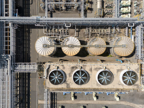 Top-down view of industrial cooling towers and large cylindrical tanks. Metal pipes and machinery surround the structures. Scene shows mechanical infrastructure, no people visible