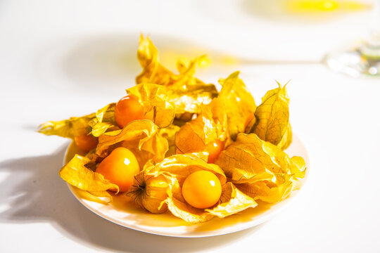 A close-up of fresh goldenberry fruits Physalis peruviana in their natural papery husks, arranged on a white plate with soft natural light.