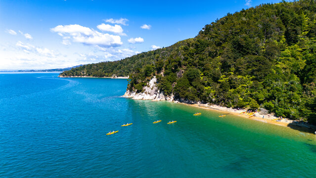 Aerial view of kayaks float on turquoise waters near lush, green cliffs, Abel Tasman National Park, Tasman Region, New Zealand.