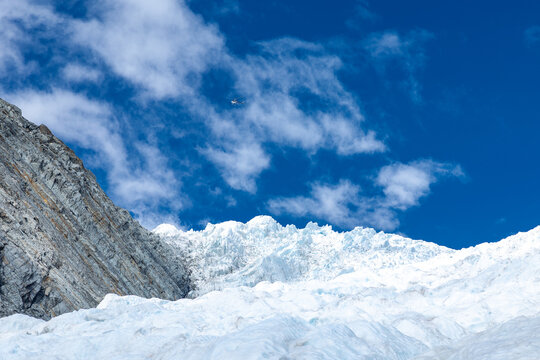 View of a dazzling white glacier cascading down a rugged mountain under a brilliant blue sky dotted with fluffy clouds, Franz Josef Glacier, West Coast Region, New Zealand.