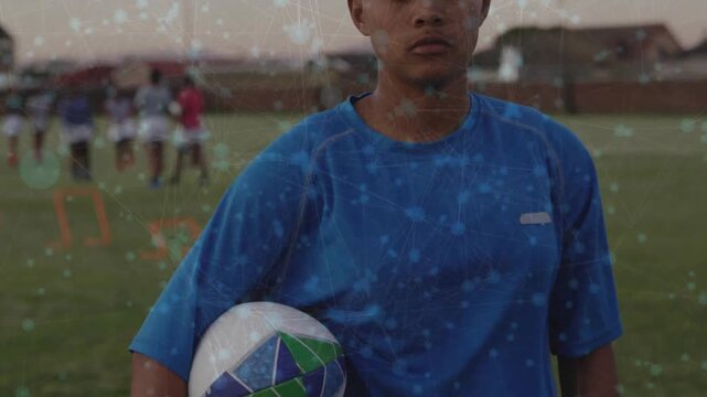 Camera panning upward revealing soccer player holding ball, team training through cones at dusk