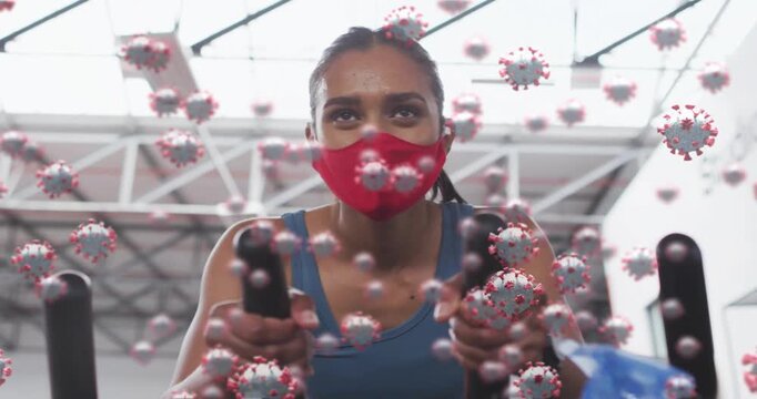 Woman gripping handlebars and initiating fitness workout in gym, virus overlay passing over face