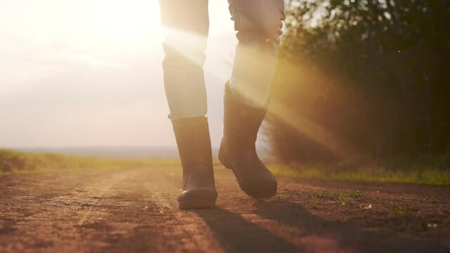 Person walking down dirt road. Man working on his boots in a field. Close lifestyle up of a farmer walking his legs up a road. An individual strolling along a gravel path.