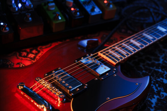 electric red sg guitar and pedalboard with pedals on carpet. blue and warm dark low key light
