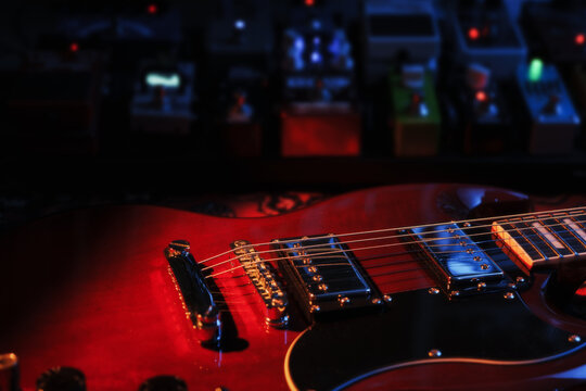 electric red sg guitar and pedalboard with pedals on carpet. blue and warm dark low key light