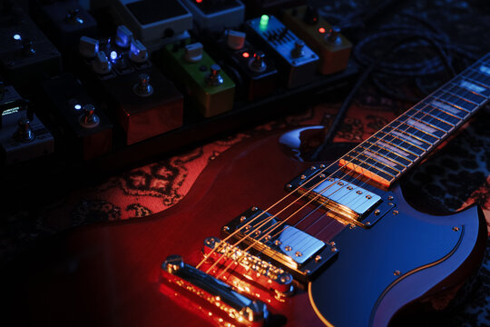 electric red sg guitar and pedalboard with pedals on carpet. blue and warm dark low key light