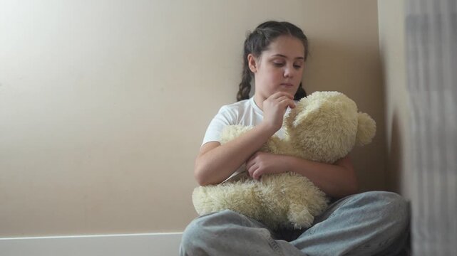 Young girl sitting on the floor with teddy bear. Teddy bear punished by sad corner. Teenage girl is traumatized by a violent attack by a teenager. A young girl is seated on the floor with a lifestyle.