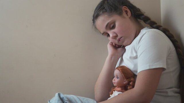 Young girl sitting on the floor with her doll. Girl punished with a doll in a corner. A teenage girl is traumatized by violence and lifestyle psychological trauma. A young girl is on the floor with.