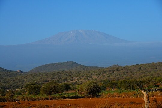 Mount Kilimanjaro viewed from the road in Kenya, rising above the African savanna under a clear sky. A scenic travel landscape featuring Africa's highest mountain and the surrounding wilderness.