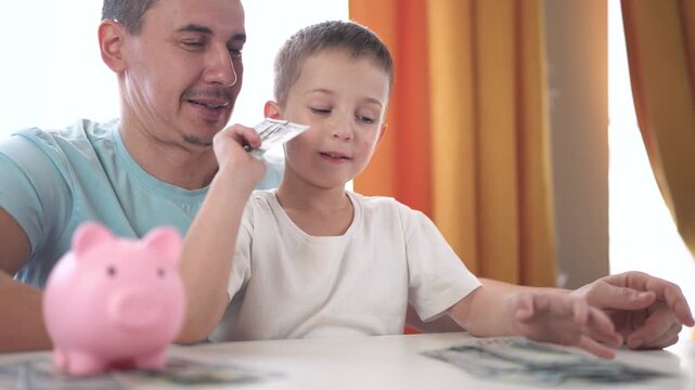 Man and little girl sitting at table with piggy bank. Family counts money lifestyle in bank. Young girl counts her sons savings. A man and a young girl are seated at a table with a piggy bank.