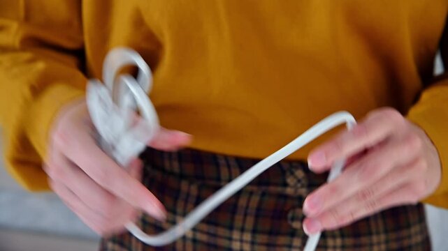 Woman organizes tangled white cords while wearing a yellow sweater indoors