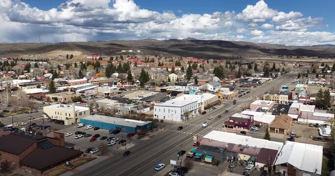 Aerial pull away from Gunnison Colorado downtown on sunny spring day with dramatic clouds