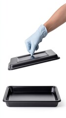 Hand in glove removing lid from black plastic tray on white background
