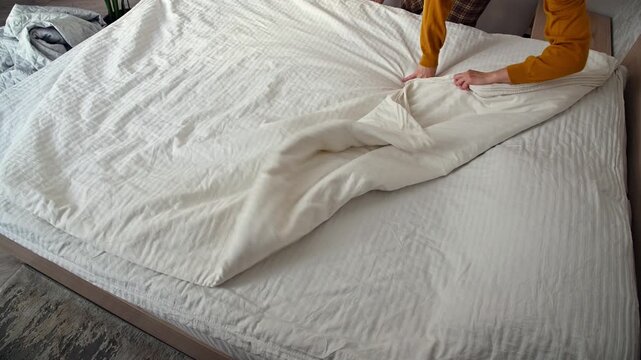Person smoothing duvet cover on bed, preparing for a tidy bedroom setup