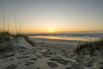 Naklejka premium Sunset over the beach with sand and grass at the water's edge in the evening