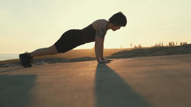 Strong athletic woman doing push-ups outdoors at sunset