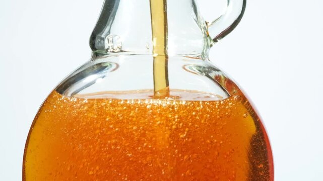 Slow motion filling glass bottle with golden maple syrup
