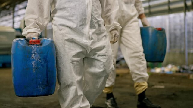 Hazmat suit industrial worker protective clothing with safety glove factory floor carrying chemical drum and chemical container hazardous material waste disposal cleanup with plastic jerrycan blue