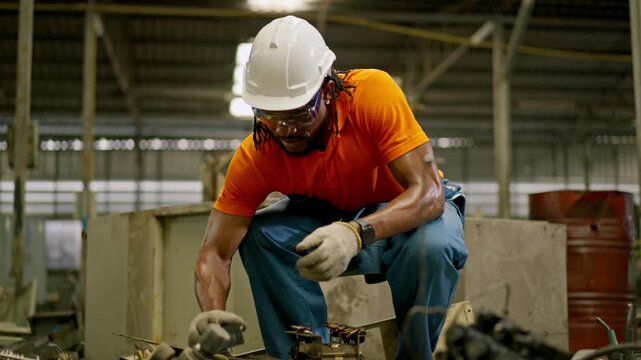 Industrial worker factory maintenance wearing hard hat safety glasses protective glove, crouching with tool for electrical repair and equipment fixing industrial warehouse, sorting metal scrap safely