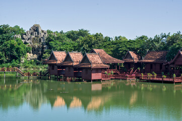 Obraz premium Picturesque traditional Khmer-style resort buildings with thatched roofs reflected in a calm ornamental lake surrounded by lush tropical gardens in Cambodia.