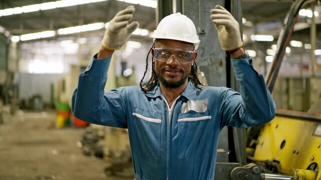 Industrial worker factory warehouse portrait, black man forklift operator hard hat safety glasses coverall glove, raising arms confidently manufacturing workshop with industrial equipment