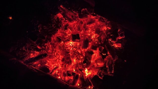Close up of glowing charcoal embers burning with red and orange tones at night. Soft heat and shimmering texture create magical atmosphere. Warm abstract scene symbolizing warmth and quiet at nature