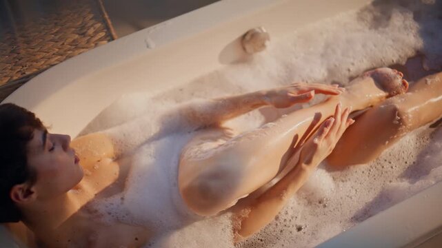 Peaceful lady relaxing bubbles bath touching skin top view. Woman lying spa