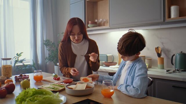 Mother with little son cook sandwiches for breakfast in kitchen