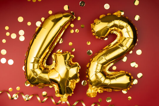 42nd birthday celebration. Gold festive balloons number 42 year anniversary on red background with confetti. Birthday or wedding event.