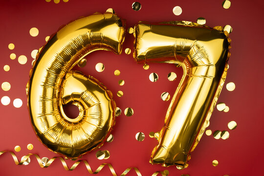 67th birthday celebration. Gold festive balloons number 67 year anniversary on red background with confetti. Birthday or wedding event.