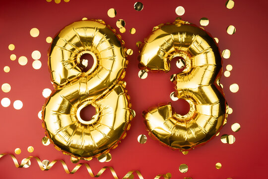 83rd birthday celebration. Gold festive balloons number 83 year anniversary on red background with confetti. Birthday or wedding event.