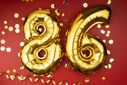 86th birthday celebration. Gold festive balloons number 86 year anniversary on red background with confetti. Birthday or wedding event.