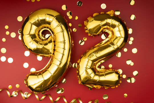 92nd birthday celebration. Gold festive balloons number 92 year anniversary on red background with confetti. Birthday or wedding event.
