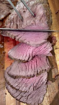 Vertical video social media - Closeup overhead shot of a hand using a knife to cut slices from a steaming hot, freshly cooked topside joint of beef, on a cutting board.