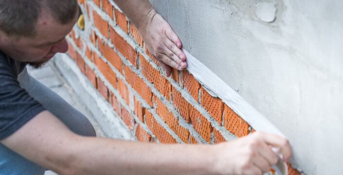 Man works carefully on brick wall foundation