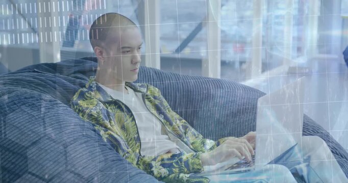 A young man is sitting in a beanbag and using a laptop computer in a modern open plan office