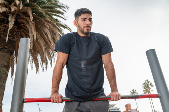Young man doing a parallel bar dip exercise, training intensely in an outdoor gym