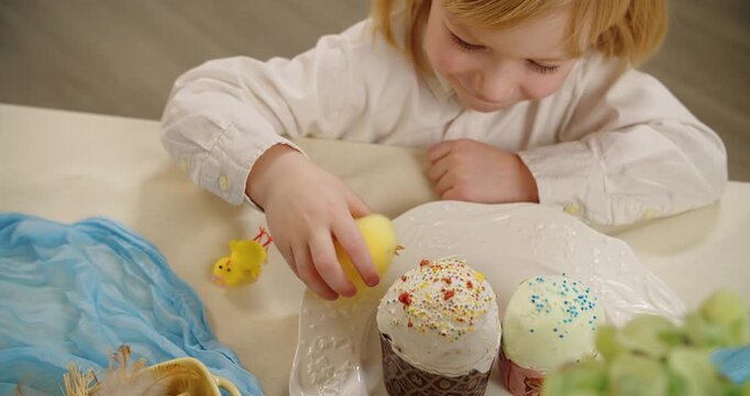 Little boy playing with toy chick near Easter cakes