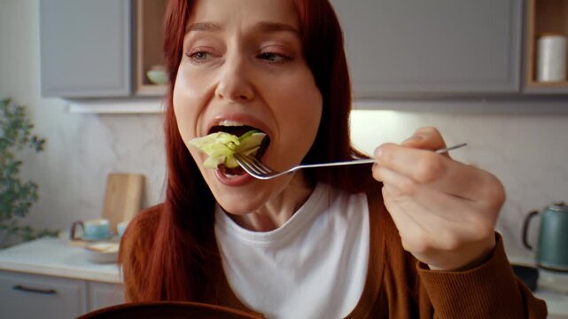 Young woman eats salad from bowl with great pleasure in kitchen