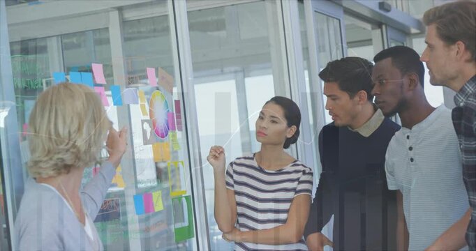 Presenter pointing at color wheel and sticky notes on glass wall, guiding team in concept mapping