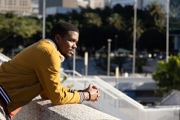 African American man leaning on concrete railing wearing jacket and white headphones, copy space © wavebreak3