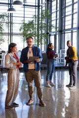 Four coworkers standing in modern office atrium, holding tablet and wearing lanyards © wavebreak3