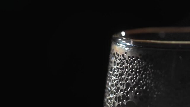 Close up of fogged drinking glass covered with condensation droplets against black background. Concepts of cold beverage, freshness, humidity, cooling, minimalism, drink styling, and studio still life