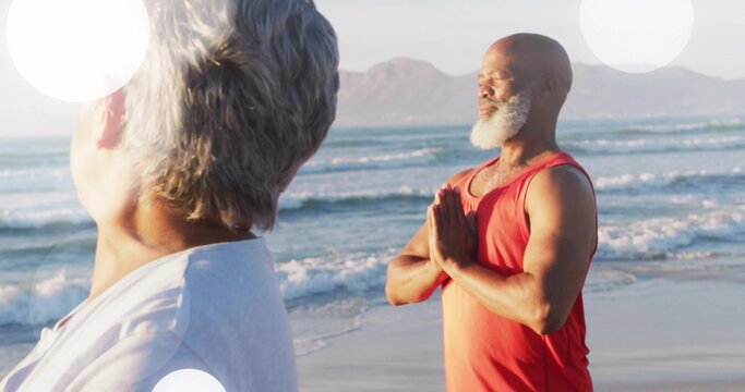 Meditating mature man holding prayer pose at sandy beach, wearing red sleeveless top, copy space
