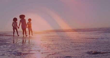 Fototapeta premium Walking woman with two children barefoot, casting reflections on wet sand on beach at sunset